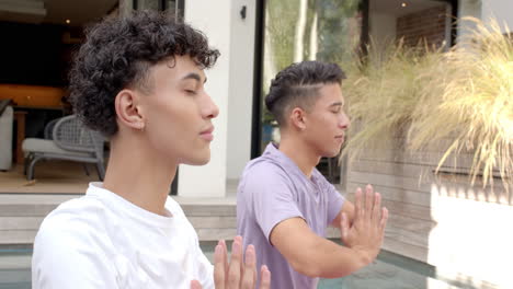 meditating, multiracial gay couple practicing mindfulness with hands in prayer position, in garden
