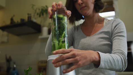 caucasian woman preparing green vegetable smoothie in kitchen