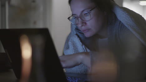 mujer cansada con anteojos estudiando tarde en la noche frente a la computadora portátil, vista estática