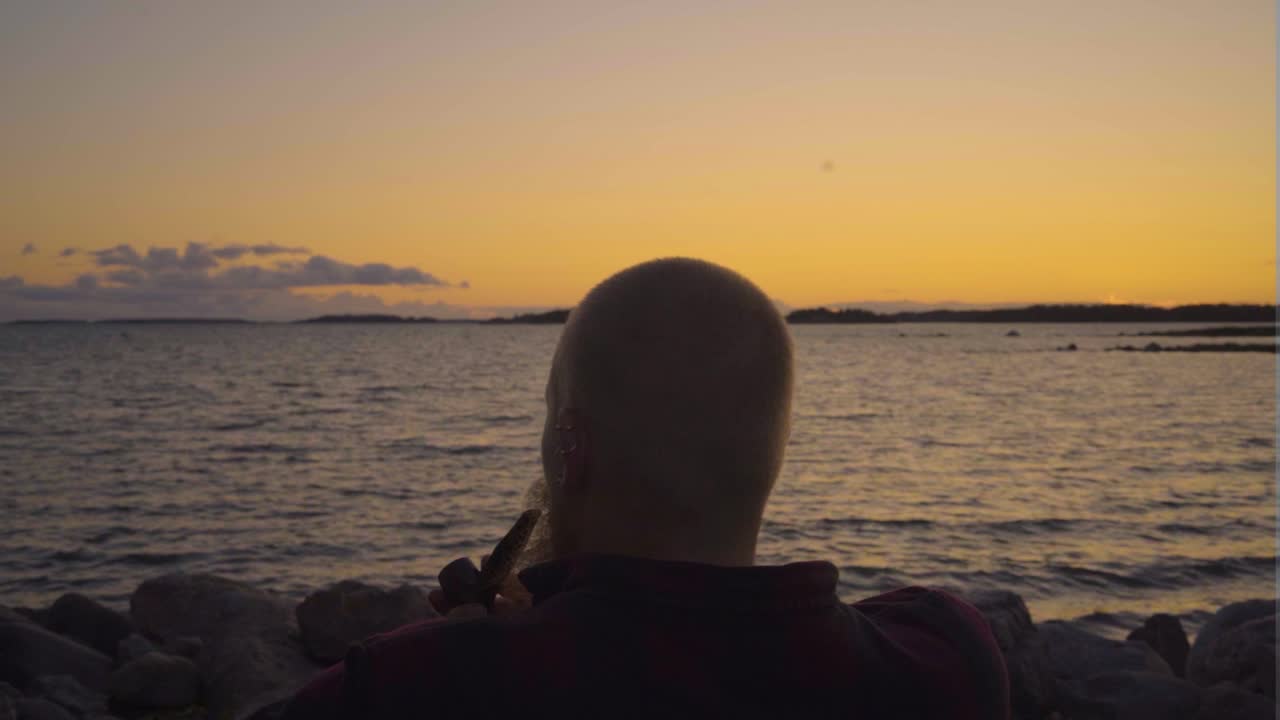 장면의 한가운데에 있는 성인 남자가 파이프를 피우며 앉아서 인생을 생각하며 물을 내려다보고 느린 움직임으로 움직이는 연기 안개 구름이 바다에서 바람과 함께 움직이고 있습니다.