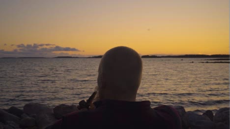 grown-male-in-the-middle-of-the-scene-sitting-down-with-his-pipe-smoking-thinking-about-life-looking-over-the-waters-moving-in-slow-motion-smoke-fog-clouds-coming-out-moving-with-the-wind-from-sea