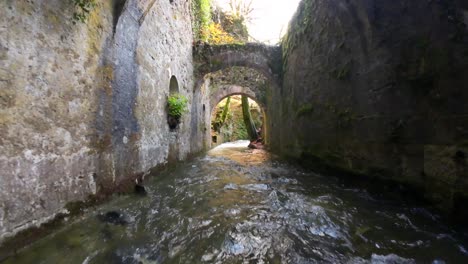 Vuelo-Del-Dron-Fpv-Sobre-Un-Río-Y-Pasando-Sobre-Los-Arcos-De-Piedra-De-Una-Antigua-Fábrica-De-Municiones-En-Eugi