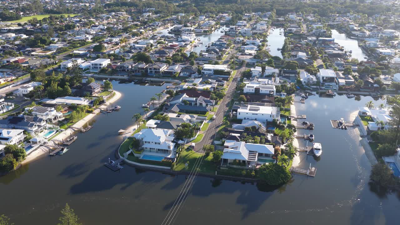 Drone footage captures serene canal-side homes in Gold Coast, Australia, under bright daylight with reflective water surfaces