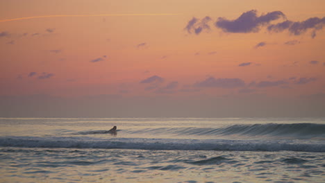 Mann-Mit-Neoprenanzug,-Der-Bei-Sonnenuntergang-Flach-Auf-Dem-Surfbrett-Im-Meer-Paddelt