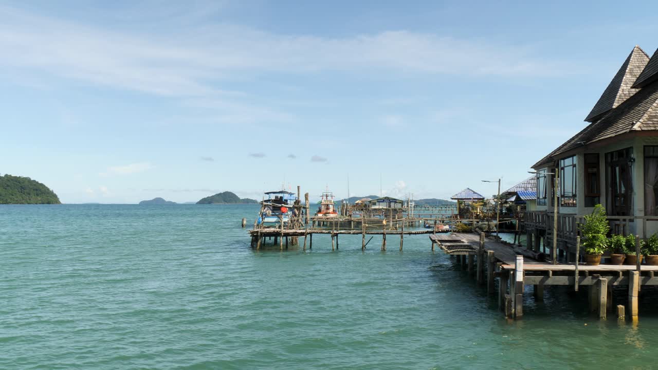 Fishing homes and seafood restaurants on wooden stilts above the sea, filmed at a fishing village in Koh Chang, Thailand, showing calm water, boats, and coastal life