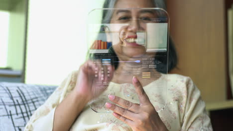 concepto de alta tecnología de una anciana asiática activa que usa una pantalla táctil transparente futurista para recibir una videollamada entrante de un miembro de la familia