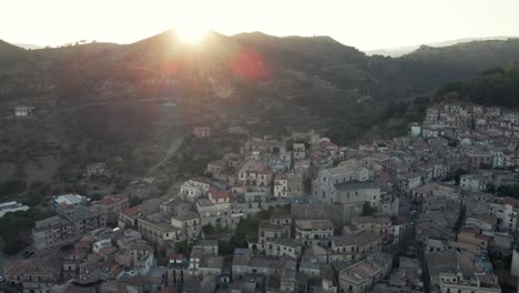 the sun sets over a mountain peak as we circle around a historic calabrian town in southern italy