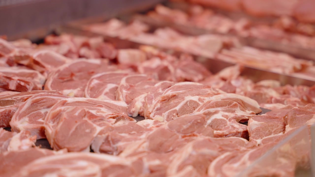 Rows of fresh raw meat slices fill a refrigerated display counter at a retail butchery.