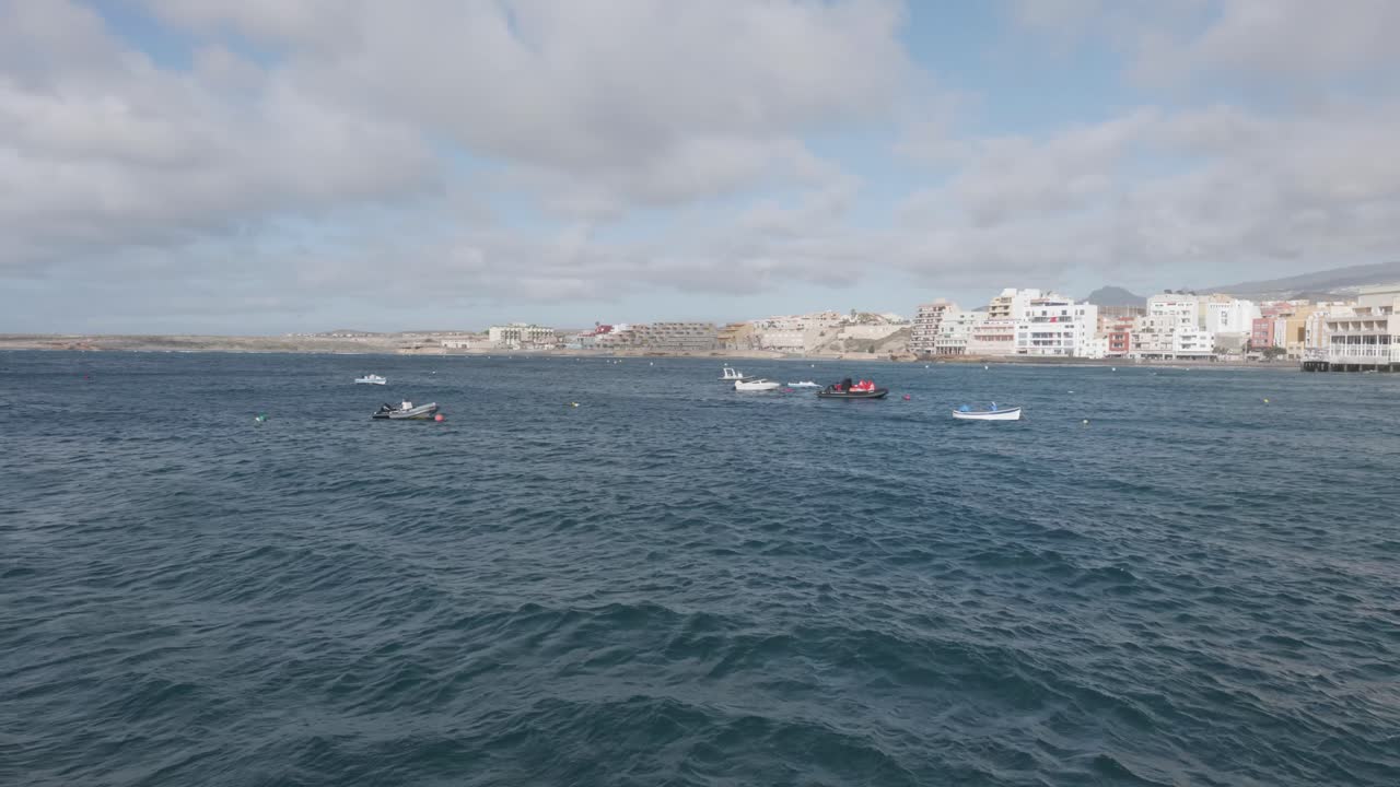 Small boats anchored by a small village by the ocean on a sunny day in El Médano, Tenerife, Canary Islands, Spain.