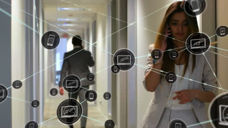 animación de una red de iconos digitales sobre una mujer de negocios biracial hablando con un teléfono inteligente en la oficina