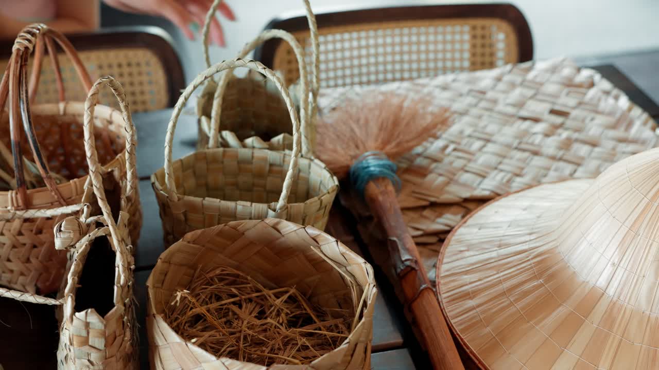 Close-up trucking shot displaying a variety of beautiful handmade woven baskets, fans, and crafts made from natural fibers at a traditional artisan workshop in Khao Lak village, Thailand