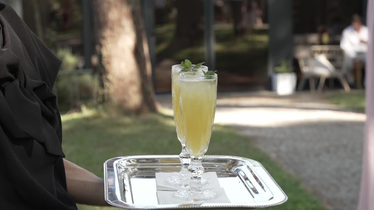 Refreshing yellow cocktail served on a silver tray with mint garnish, outdoor setting