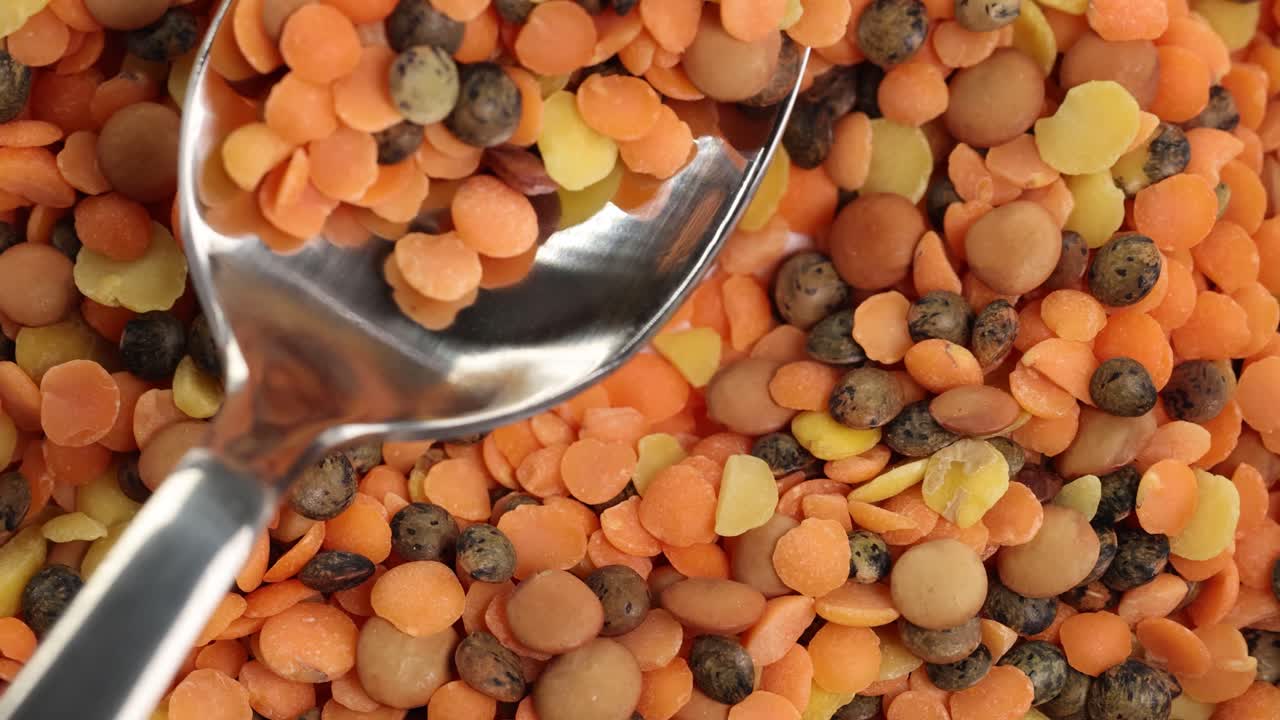 A spoon moves through a vibrant mix of lentils and chickpeas, highlighting texture and color in close-up detail