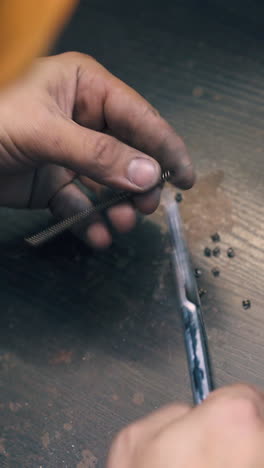 cu: professional jeweler cuts parts from gold metal spiral over wooden table in light craft workshop close view
