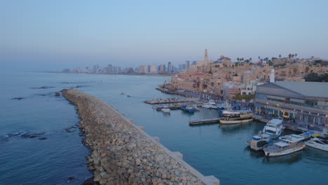 jaffa port and the old city at sunset with lots of families visiting restaurants, shops and bars in the port, tel aviv towers in the background - push in drone shot