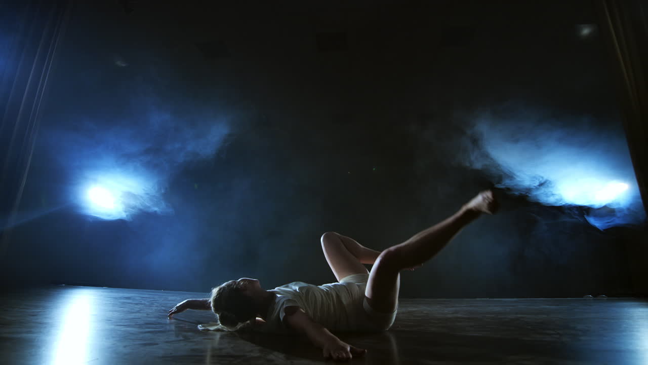 Movimento lento: Donna che balla balletto moderno a piedi nudi, sdraiata a terra, esegue giri, piroette e capriole.