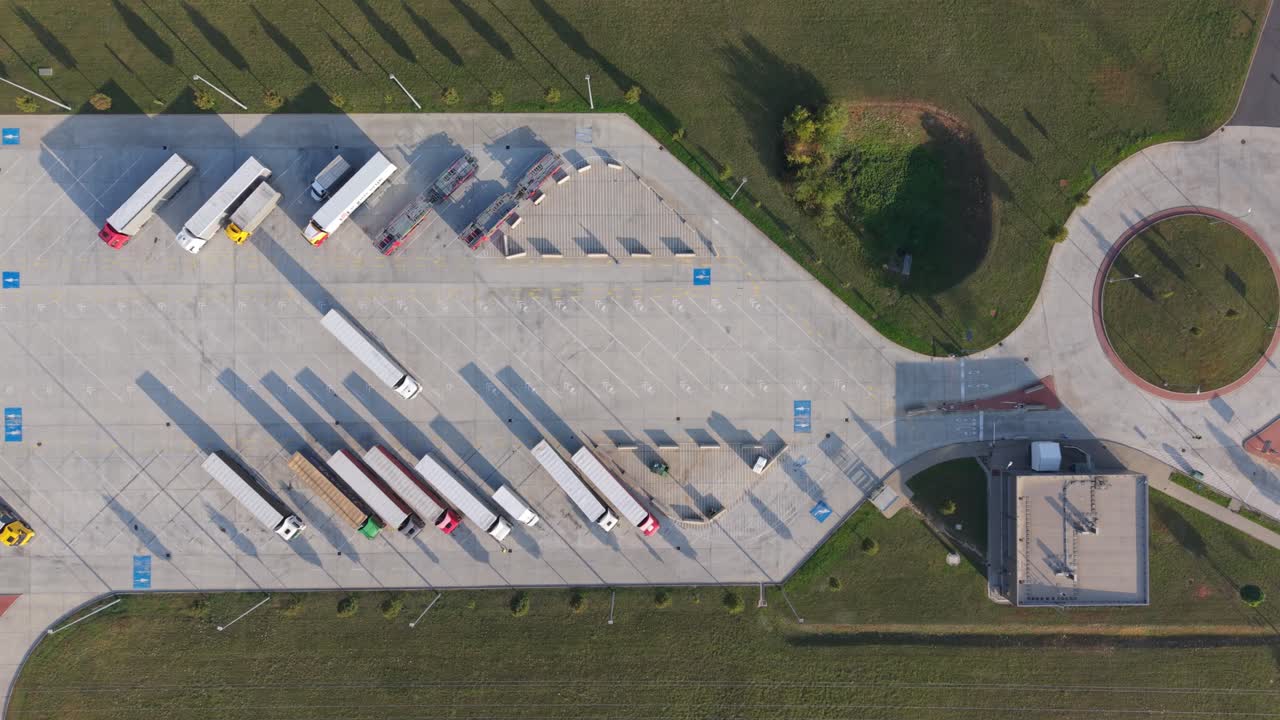 A top-down aerial view of a large truck parking lot showing multiple semi-trailers parked in designated spaces. Drone flying over the parking lot