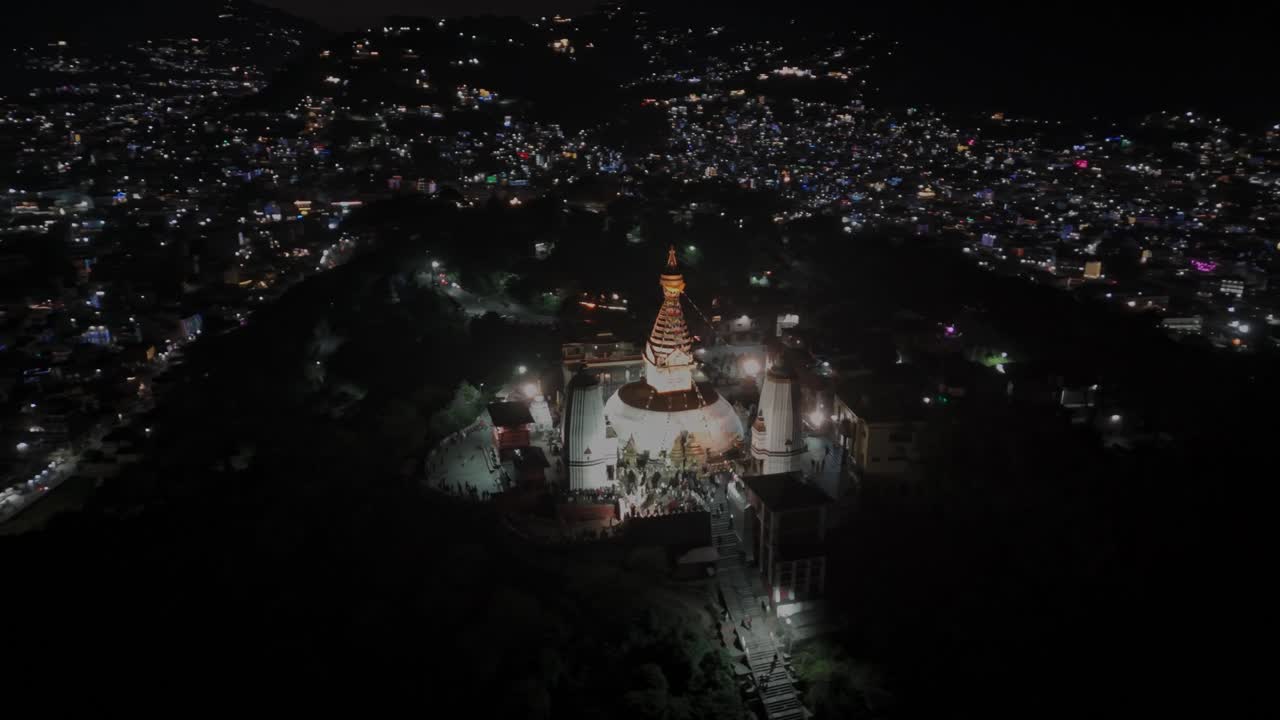 Filmato aereo notturno con drone dello stupa di Swayambhunath a Kathmandu, illuminato da luci calde in cima alla collina, che ne mostra l'atmosfera spirituale e l'iconica architettura buddista