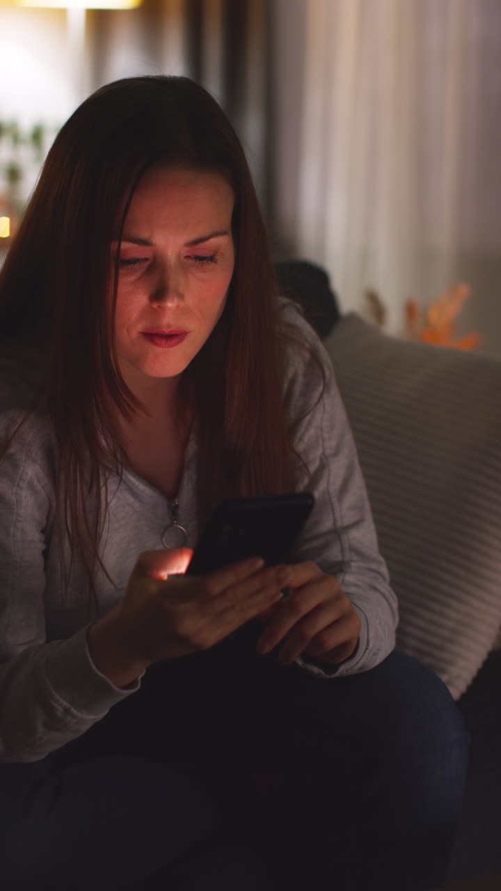 Vertical Video Of Anxious Woman Lying On Sofa At Home Looking At Mobile Phone Concerned About Social Media Or Bad News