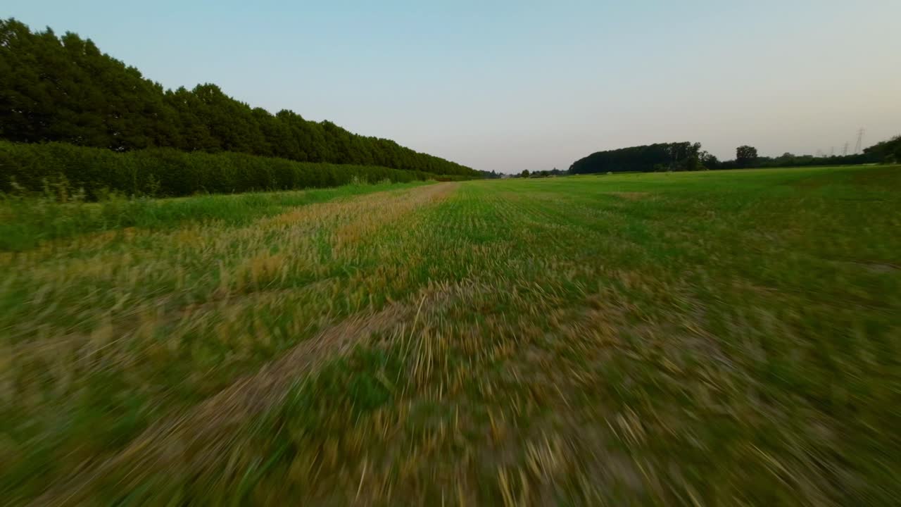 drone fpv volando a alta velocidad sobre amplios campos y prados verdes al atardecer