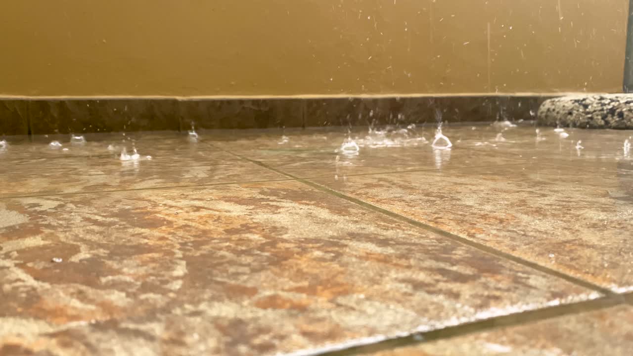 Gotas de lluvia caen sobre el suelo de baldosas del balcón, formando charcos y burbujas