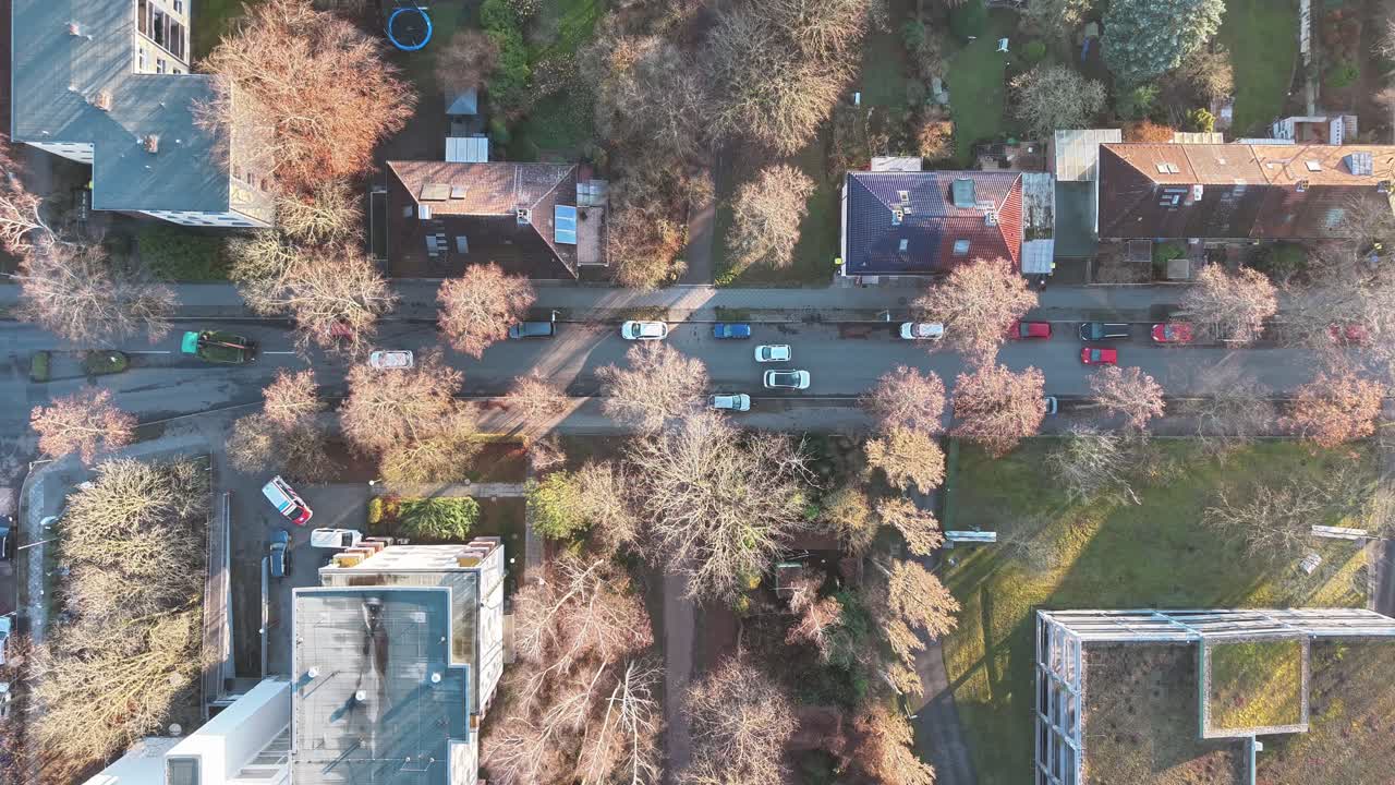 A top-down drone shot captures a tranquil suburban street in Berlin, featuring parked cars, colorful trees, and residential buildings