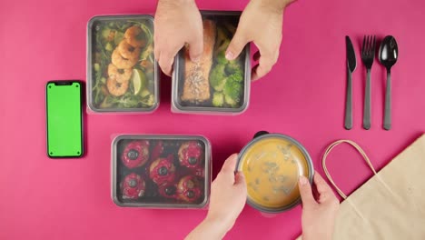 food delivery top view, take away meals in disposable containers on pink background. lunch boxes with cooked vegetarian dishes, phone with chroma green screen. healthy diet. catering service