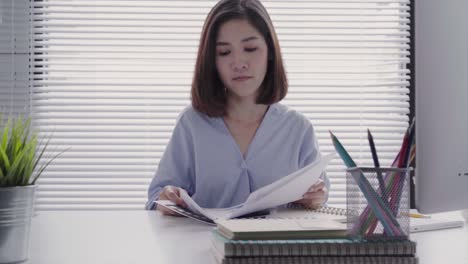 beautiful young smiling asian woman working on laptop while sitting in a living room at home. asian business woman working in her home office. enjoying time at home.