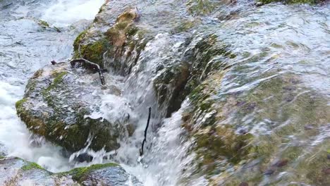 Panning-view-of-water-cascading-along-a-rocky-surface-with-moss-and-autumn-leaves-on-the-bottom-in-Plitvice-Lakes-National-Park-in-Croatia,-Europe-at-¼-speed