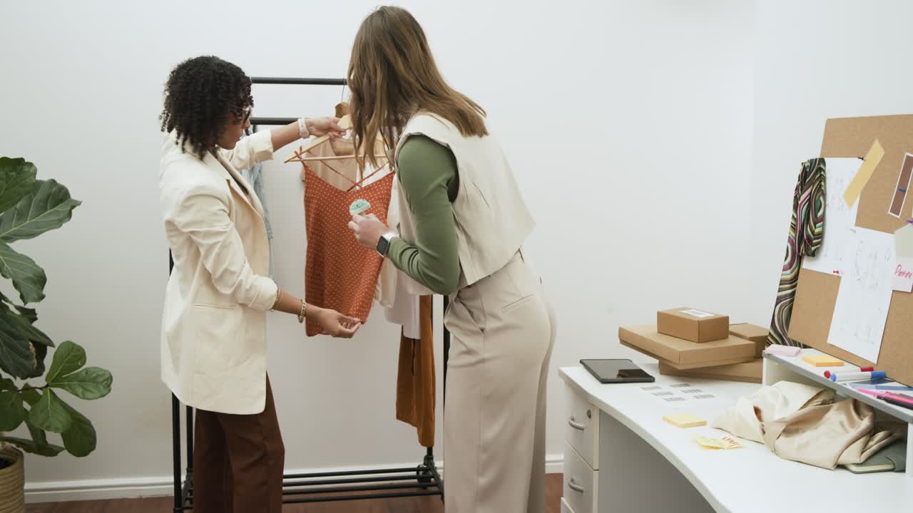 Designer donne di diverse etnie che sollevano una blusa da uno stand e confrontano le spalline di una canotta lavorando in studio.