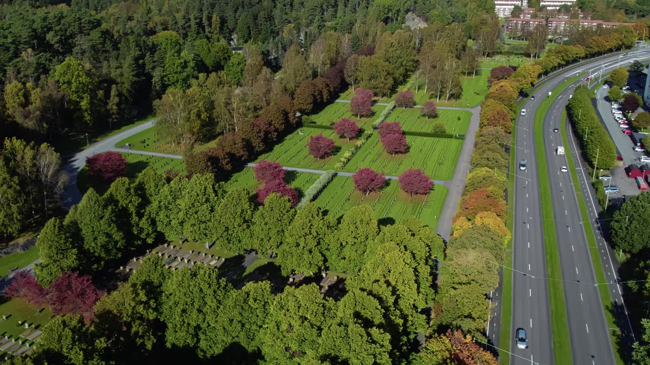 High angle aerial view of Kviberg Cemetery with red leaved trees, grave plots, and multi-lane road in Gothenburg, Sweden
