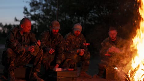 the military set up camp at night in the training areas, lit a campfire to warm up and frying sausages on sticks, the men were on duty, guarding the training ground, talking among themselves