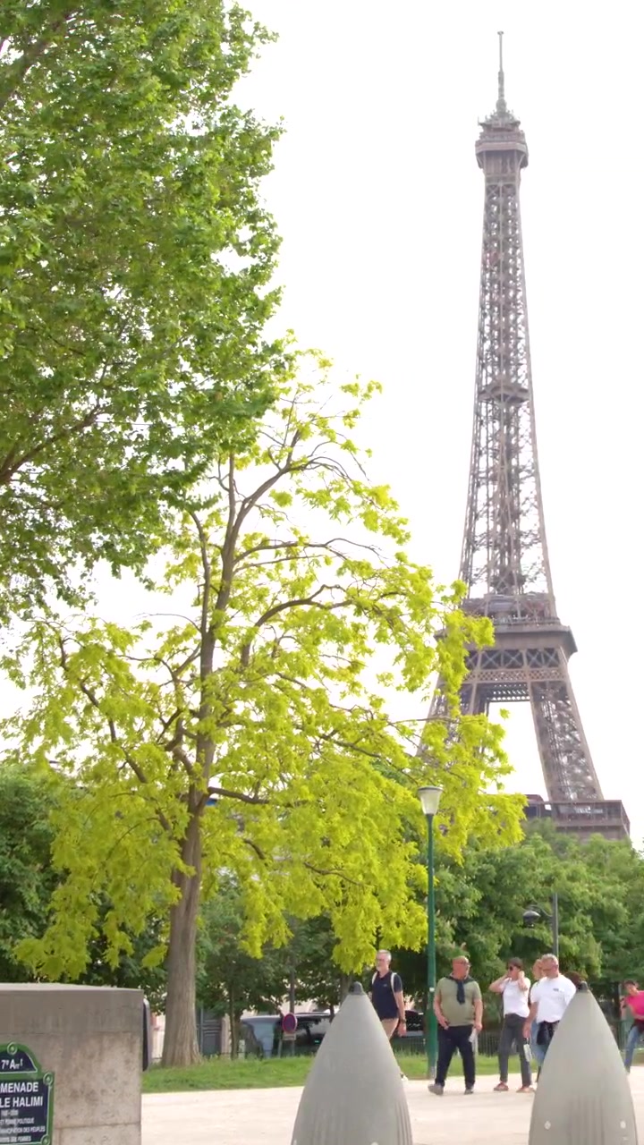 La telecamera si sposta lentamente attraverso un parco soleggiato a Parigi dove i turisti camminano vicino alla Torre Eiffel