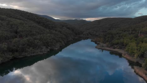 Toma-Aérea-Rápida-Sobre-Un-Lago-De-Montaña,-Aguas-Tranquilas-Que-Reflejan-El-Bosque-De-Nubes-Del-Atardecer.