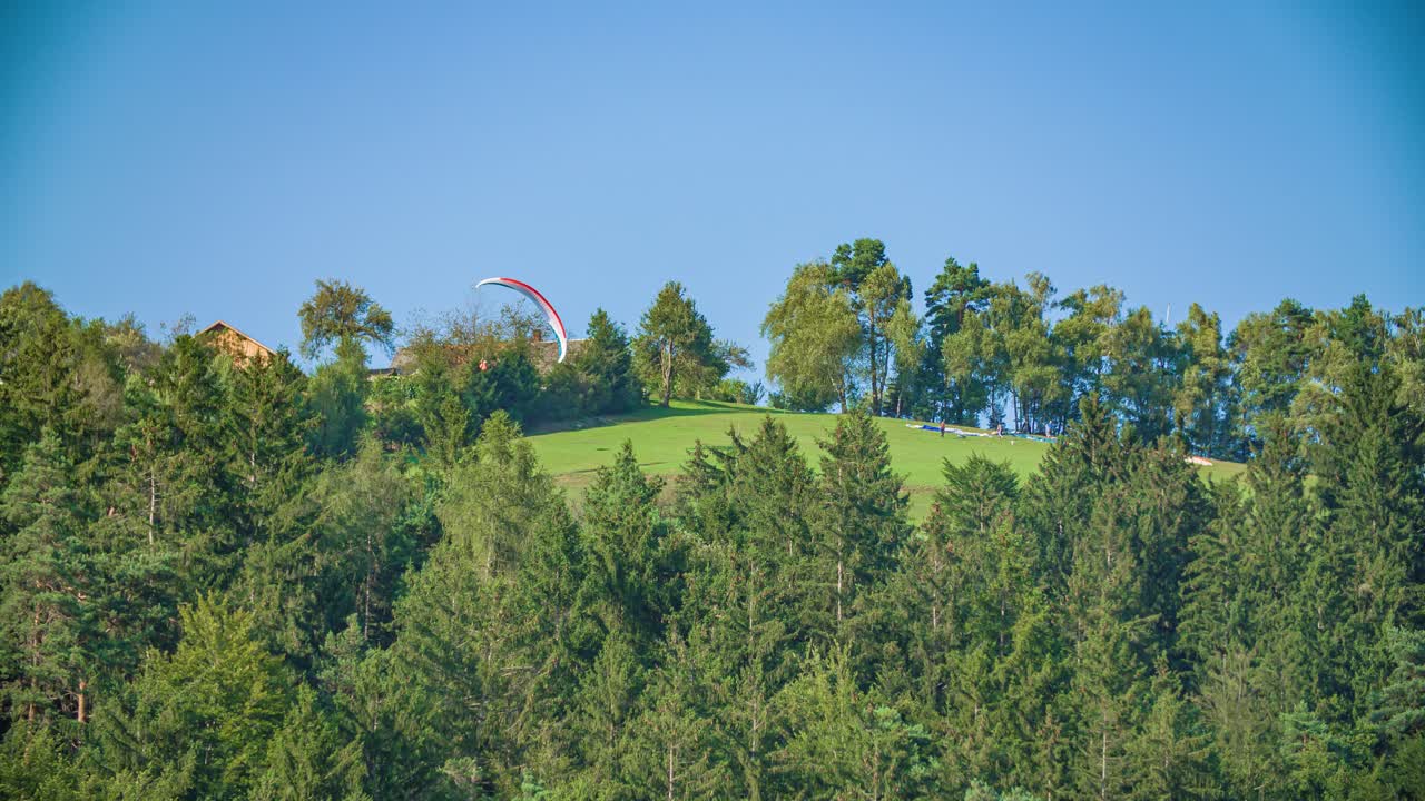 Paraglider pilot making flight manoeuvres with hill and forest in background