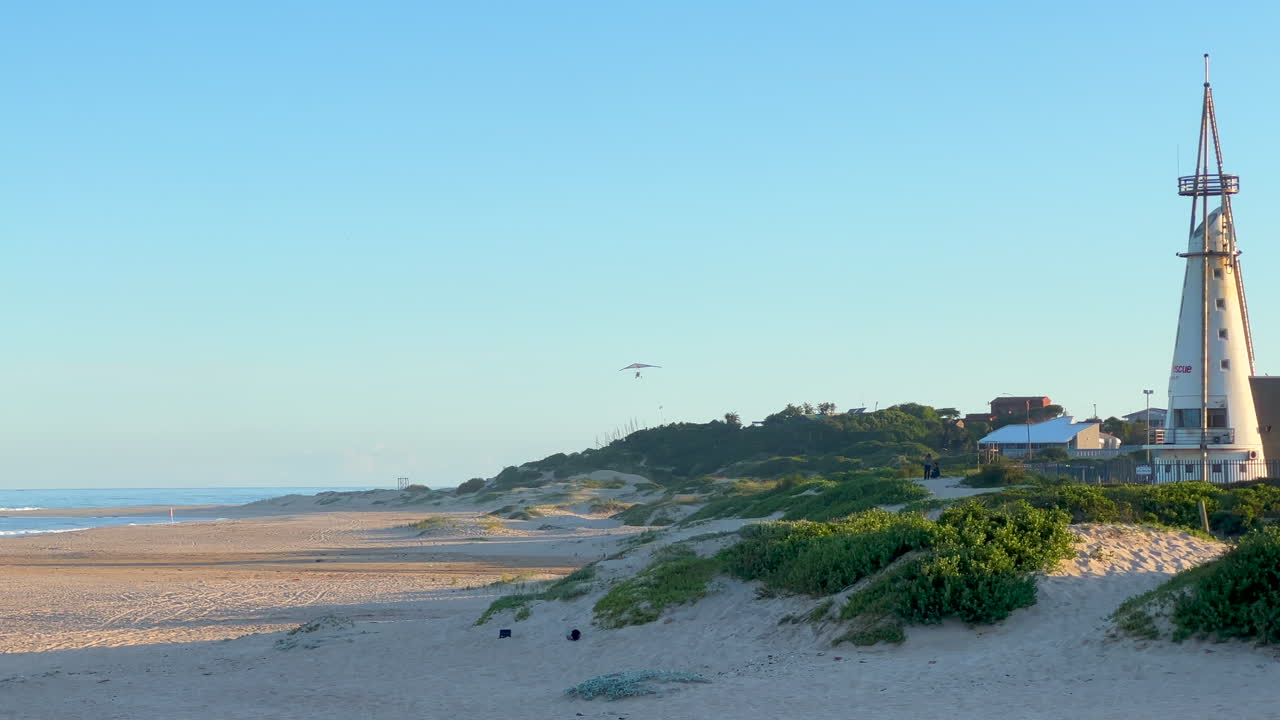 Glider flying by Jeffrey's Bay Lighthouse South Africa WSL JBAY Corona Open Supers Boneyard downtown main tourist beach late afternoon sunset mid summer slow motion pan to the left