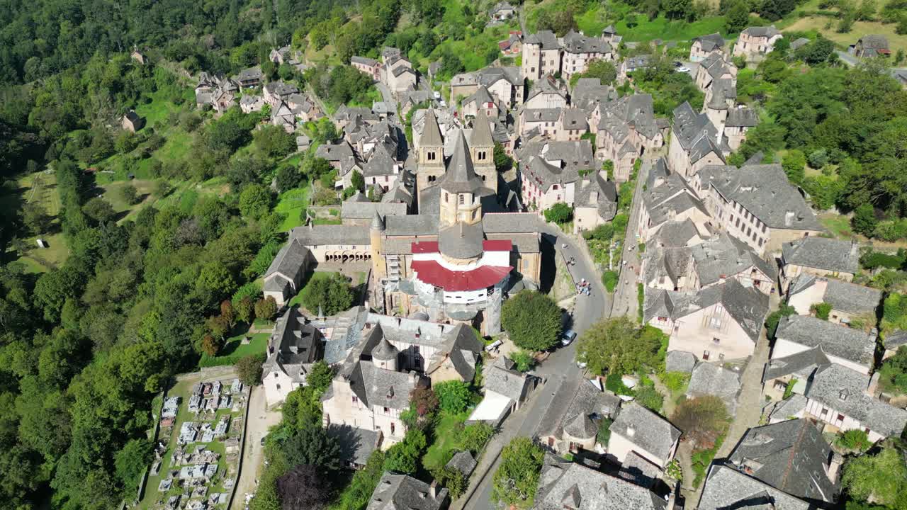 Drone aerial view in France countryside small old medieval town and a cathedral surrounded by a green mountain forest flying over in Conques
