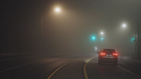 vehicles driving away on misty road at night - wide