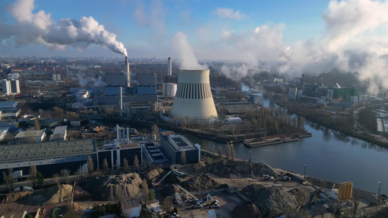 power plant emitting steam from its cooling tower, situated by a river and overlooking the cityscape. Unique aerial view flight static tripod hovering drone