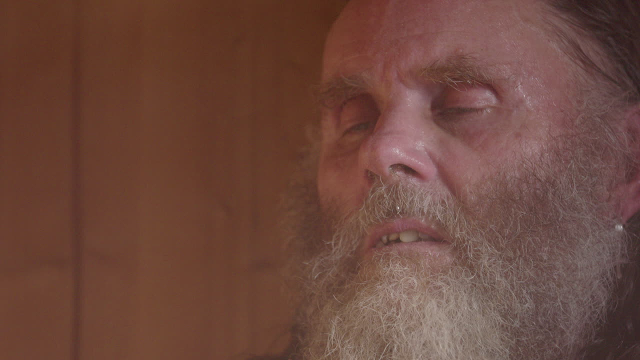 Meditative hippy man with lots of facial hair eyes half closed in steamy sauna