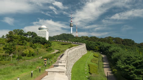 seoul city wall in namsan park and n tower against blue sky with floating clouds, korean people walking up and down on mountain trails on summer day