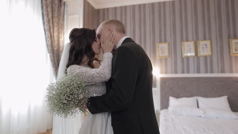 Newlyweds-young-caucasian-bride-and-groom-first-meeting-at-wedding-day,-making-a-kiss-indoors