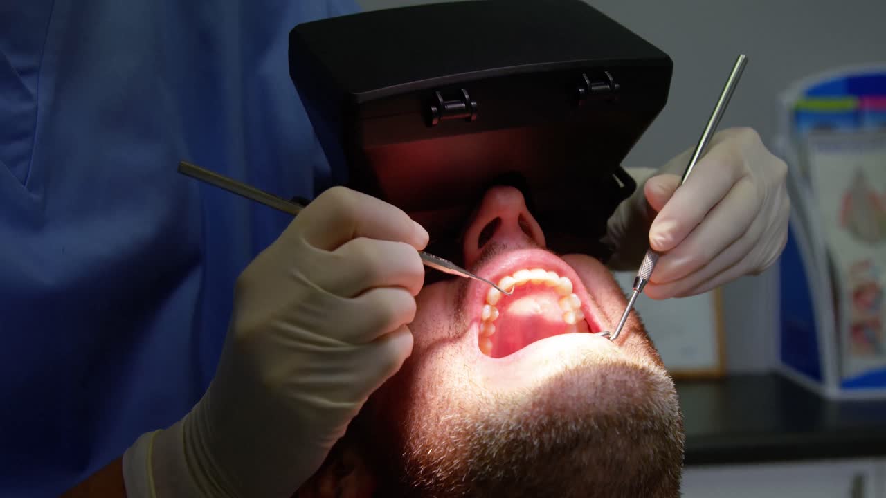치과 의사 가 치과 도구 를 사용 하여 남성 환자 를 검사 하고 있다