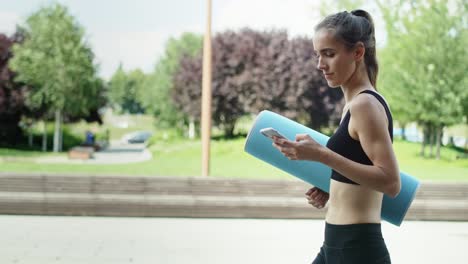 Video-of-woman-with-phone-walking-in-training-clothes-outdoors