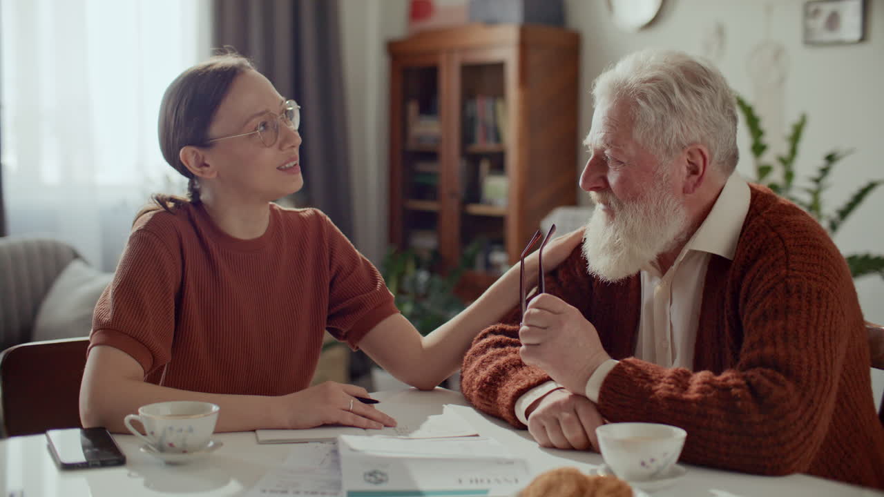 Woman Supporting Elderly Grandfather and Helping Him with Bills at Home