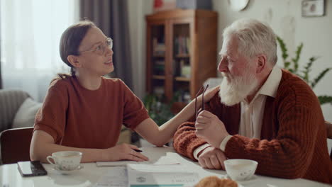 woman supporting elderly grandfather and helping him with bills at home