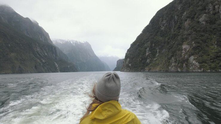 Mädchen in leuchtend gelber Regenjacke steht am Heck eines Bootes, das an einem regnerischen und kalten Tag durch die Fjorde Neuseelands fährt.