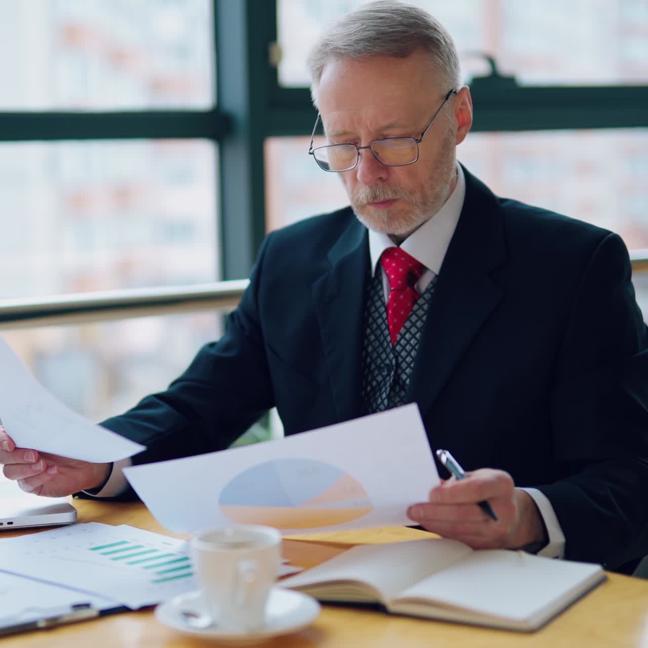 Thoughtful businessman is reading important business papers, video in front of the window with city view. Video of business process.