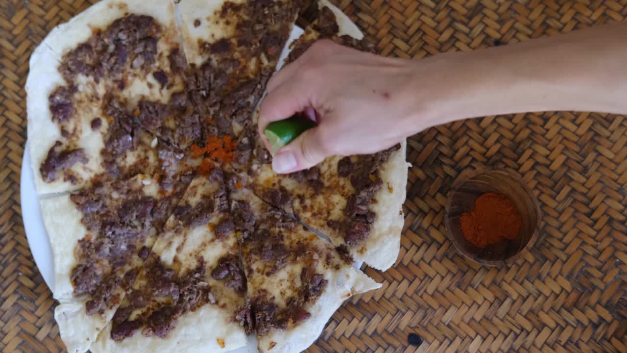 cerca de una mano exprimiendo lima y poniendo especias en manakish lahm bi ajeen - panes planos con cordero picado o carne de res y pastel relleno de fatayer con espinaca. comida árabe tradicional