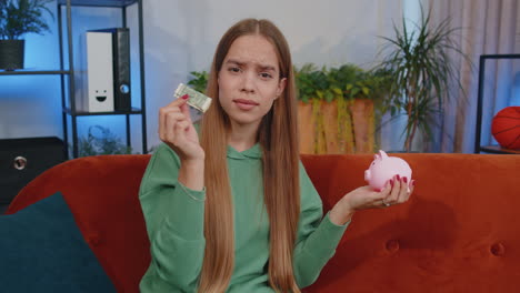 poor young girl holding piggybank and one dollar banknote, financial crisis, bankruptcy, poverty